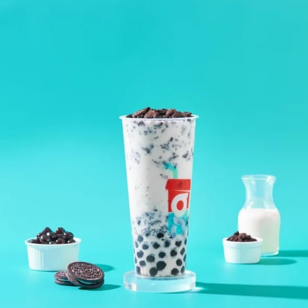 Oreo bubble tea with crushed Oreos, whole Oreos, milk, and chocolate chips on a blue background.