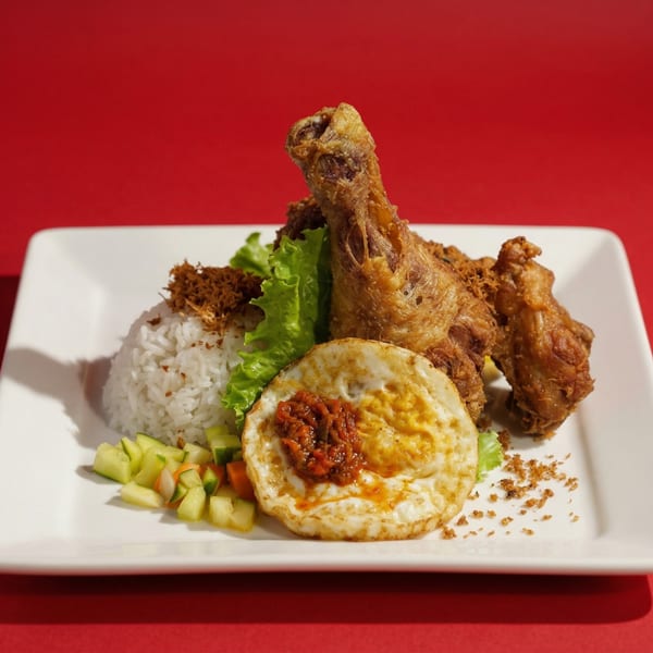 Crispy fried chicken with rice, fried egg, sambal, and pickled vegetables on a white plate.